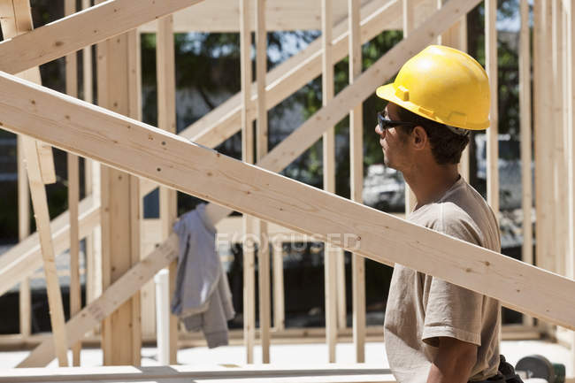 Carpenter standing under a framed house at a building construction site — Stock Photo