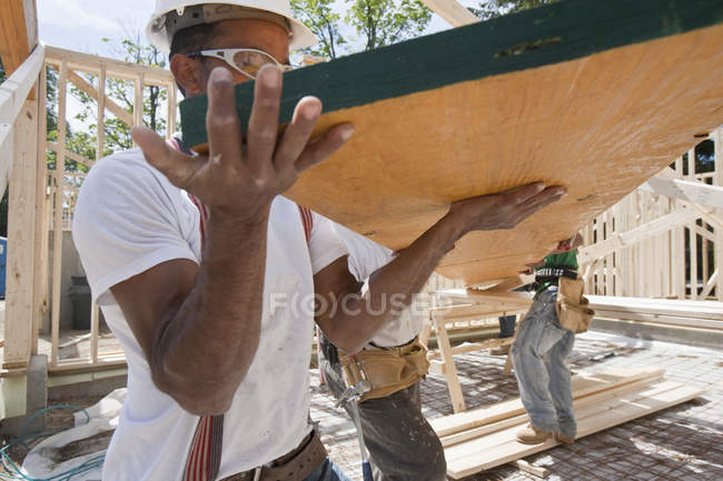 Charpentiers soulevant une poutre laminée sur un chantier de construction — Photo de stock