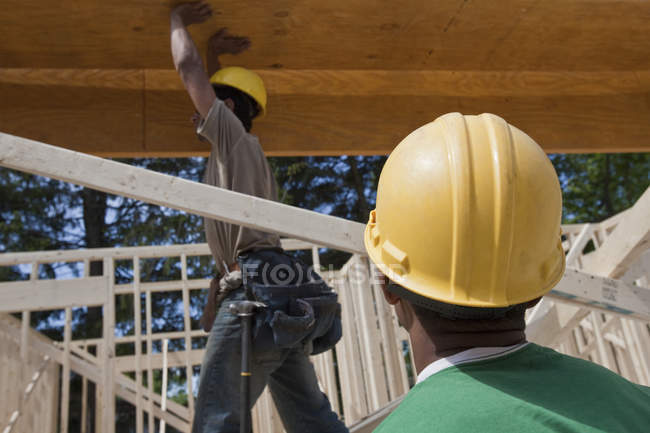 Charpentier soulevant une poutre laminée sur un chantier de construction — Photo de stock