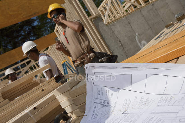 Construction plan with carpenters framing a house — Stock Photo
