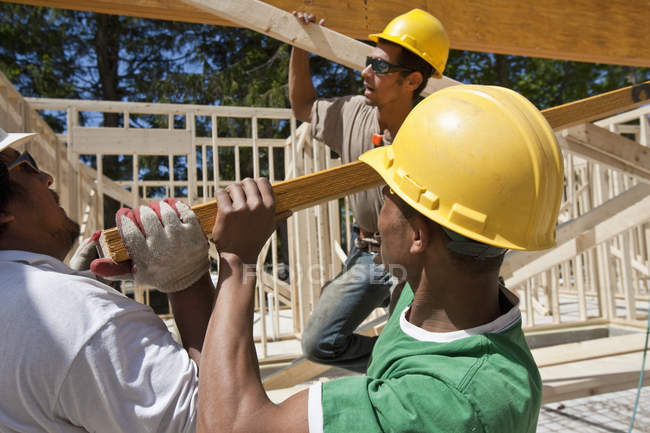 Carpinteiros levantando um feixe laminado em um canteiro de obras — Fotografia de Stock