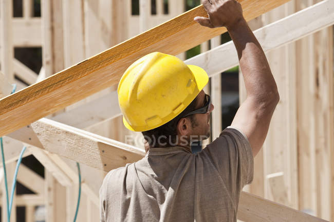 Charpentier soulevant une poutre laminée sur un chantier de construction — Photo de stock