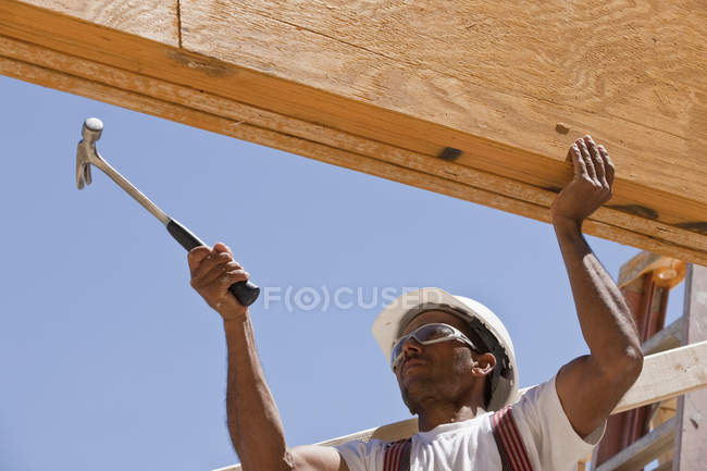 Carpintero martillando una viga en un sitio de construcción de edificios - foto de stock