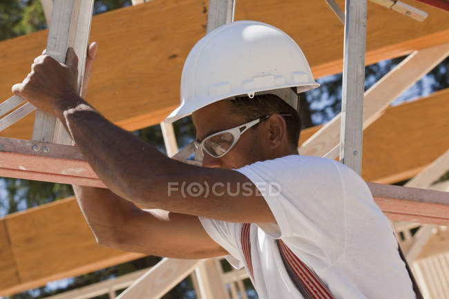 Carpenter carrying a ladder at a building construction site — Stock Photo