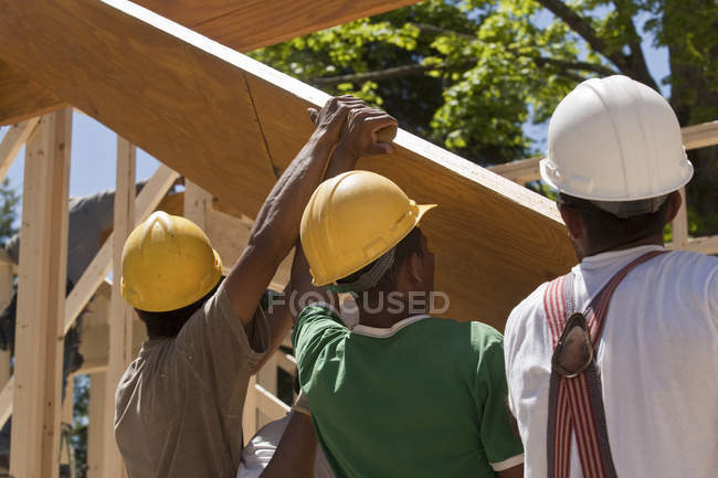 Carpinteiros levantando feixe em um canteiro de obras — Fotografia de Stock