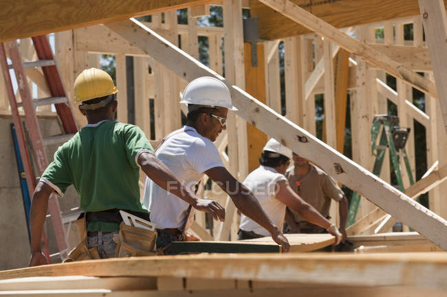 Carpinteiros levantando feixe em um canteiro de obras — Fotografia de Stock