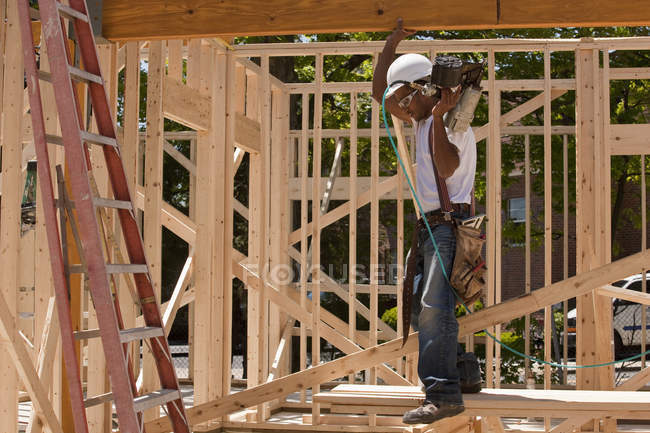 Carpenter standing at a construction site holding a nail gun — Stock Photo