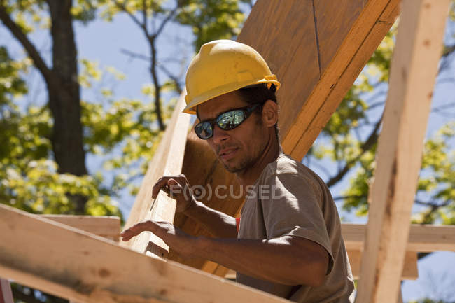 Charpentier soulevant une poutre sur un chantier de construction — Photo de stock