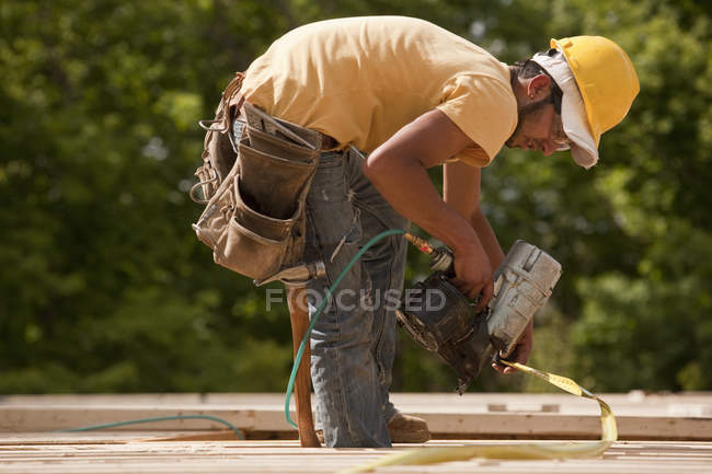 Carpinteiro usando pistola de prego em madeira e quadro de medição — Fotografia de Stock