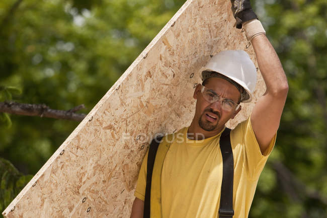 Charpentier portant un panneau de particules sur un chantier de construction — Photo de stock