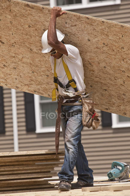 Carpinteiro carregando uma placa de partículas em um canteiro de obras — Fotografia de Stock