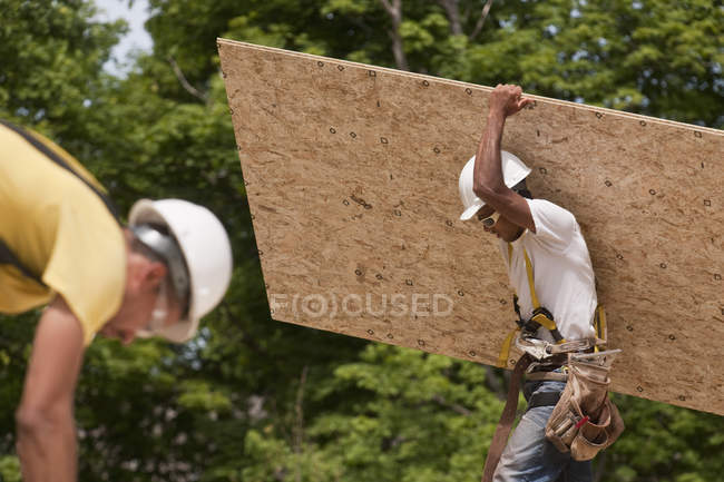Carpinteiros que transportam uma placa de partículas num estaleiro de construção — Fotografia de Stock