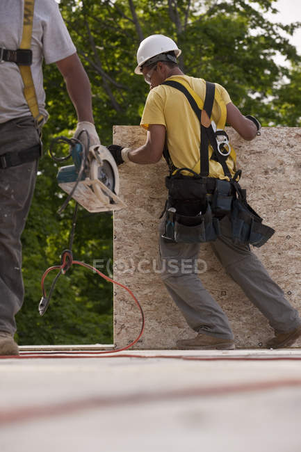 Carpenters lifting particle board and holding circular saw — Stock Photo
