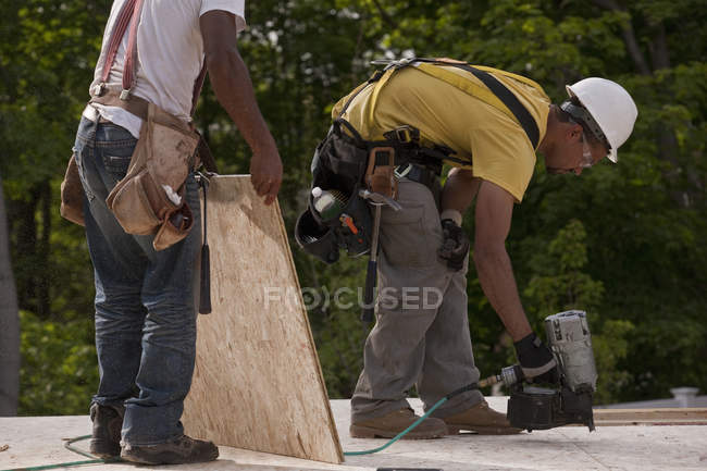 Carpinteros clavando un tablero de partículas en un sitio de construcción de edificios - foto de stock