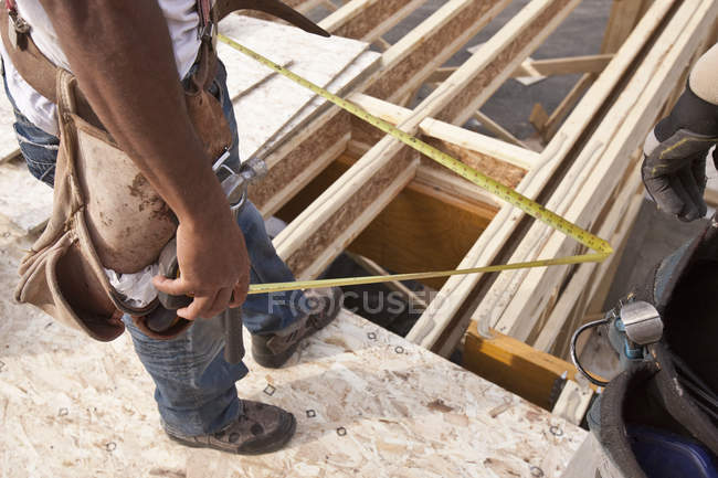 Carpintero sosteniendo una cinta métrica en una obra de construcción - foto de stock