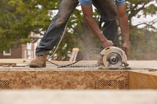 Charpentier sciant un panneau de particules sur un chantier de construction — Photo de stock