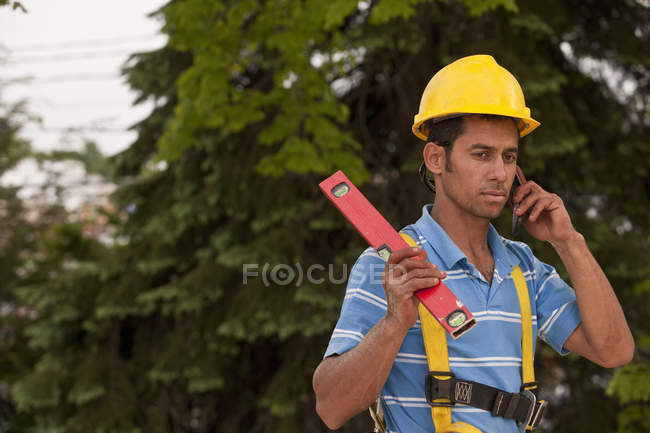 Carpenter holding a level and talking on a mobile phone — Stock Photo