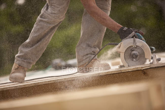 Cropped image of carpenter sawing a board at a building construction site — Stock Photo