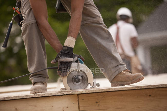 Imagen recortada de Carpenter aserrando una tabla en un sitio de construcción de edificios - foto de stock