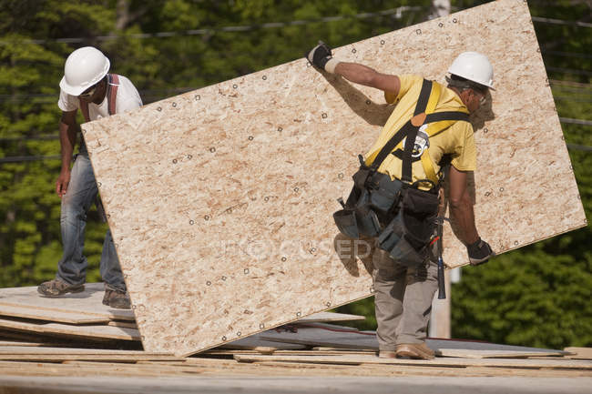 Carpinteros moviendo un tablero de partículas en un sitio de construcción de edificios - foto de stock