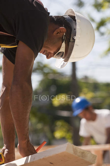 Плотники пишут измерения по дереву на строительной площадке — стоковое фото