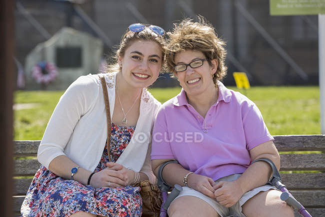 Mujer con parálisis cerebral sentada con su hermana en un parque - foto de stock