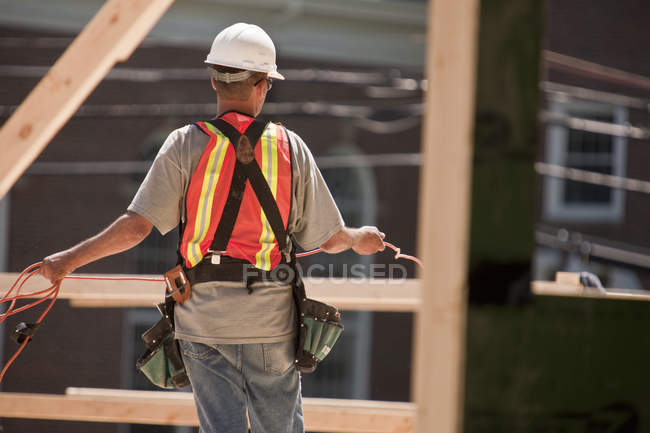 Charpentier enroulant un câble d'alimentation sur un chantier de construction — Photo de stock