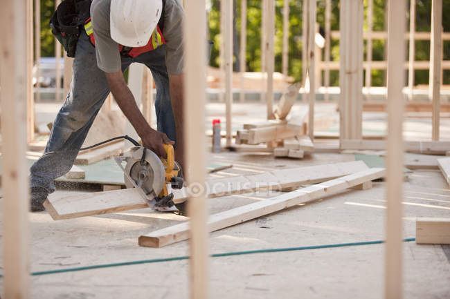 Плотник режущий раму с циркулярной пилой на строительной площадке здания — стоковое фото