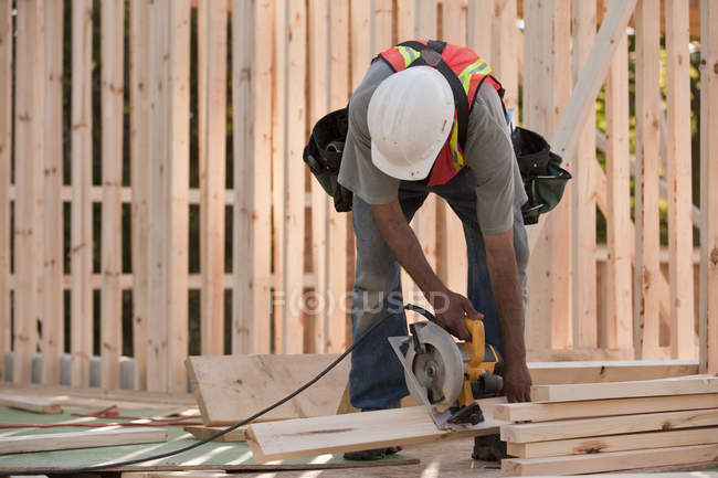 Carpenter sawing wood for house framing at a building construction site — Stock Photo
