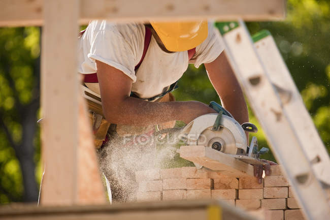 Carpintero aserrando una madera en un sitio de construcción de edificios - foto de stock