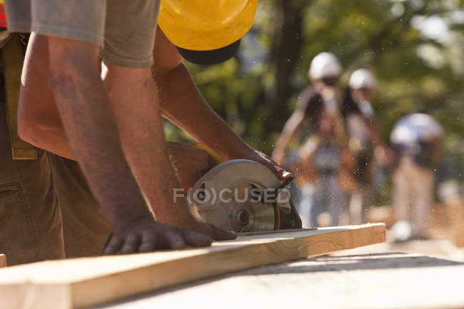 Carpinteros usando una sierra circular en un sitio de construcción - foto de stock