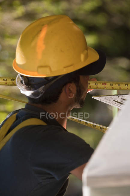 Carpinteiro usando uma fita métrica em um canteiro de obras — Fotografia de Stock