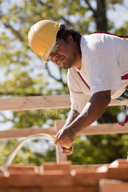 Плотник измеряет доски лентой на строительной площадке — стоковое фото