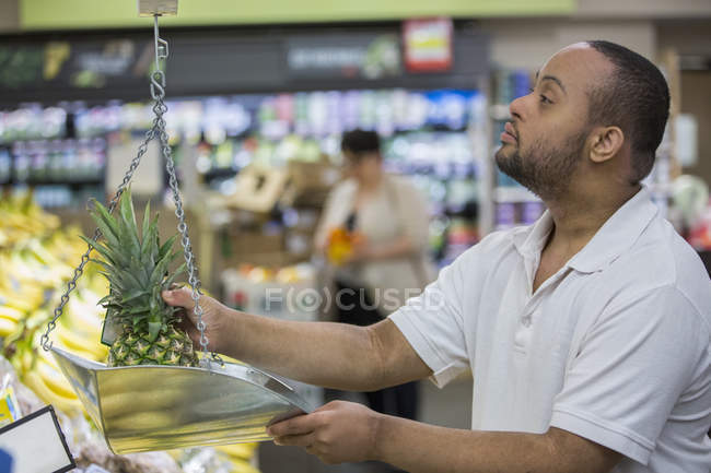 Man with Down Syndrome weighing pineapple in a grocery store — Stock Photo