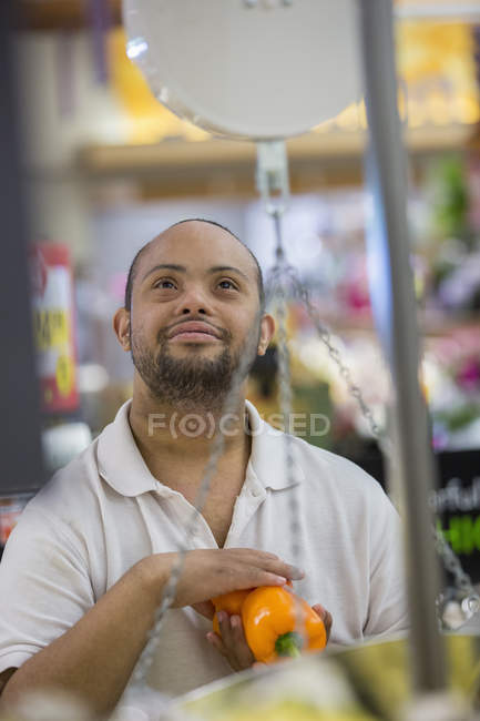 Man with Down Syndrome weighing vegetable in a grocery store — Stock Photo