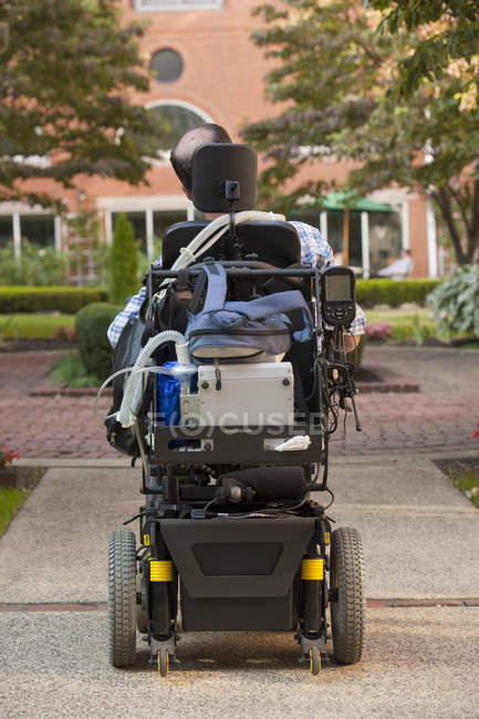 Rear view of a man with Duchenne muscular dystrophy in a motorized wheelchair on the street — Stock Photo