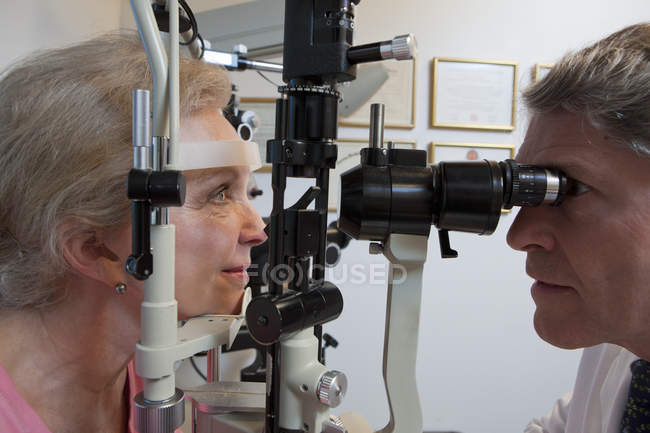 Oftalmologista examinando os olhos de uma mulher com uma lâmpada de fenda — Fotografia de Stock