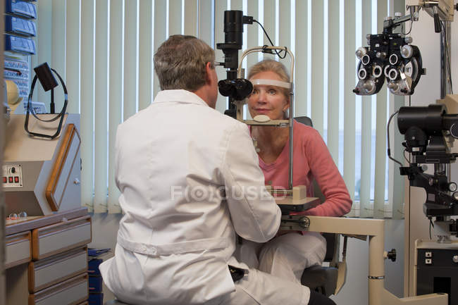 Oftalmólogo examinando los ojos de una mujer con una lámpara cortada - foto de stock