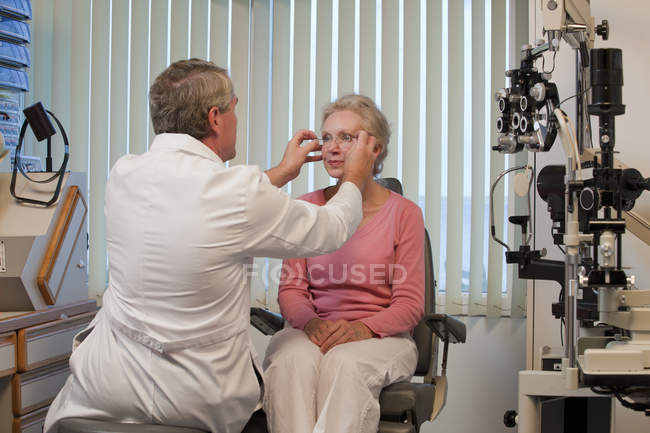 Oftalmólogo ajustando gafas a los ojos de una mujer - foto de stock