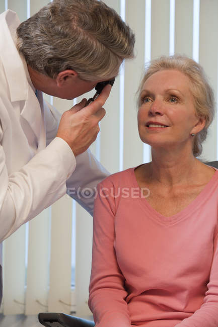 Oftalmólogo examinando los ojos de una mujer con un oftalmoscopio directo - foto de stock