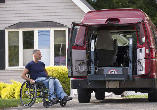 Hombre con lesión medular en una silla de ruedas subiendo a su furgoneta accesible - foto de stock