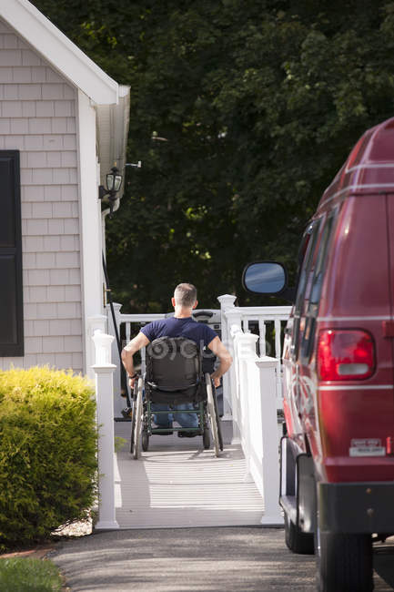 Hombre con lesión medular en una silla de ruedas subiendo a su casa rampa - foto de stock