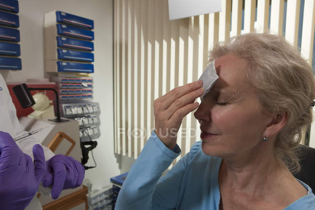 Patient applying ice on her forehead after a Botox treatment — Stock Photo