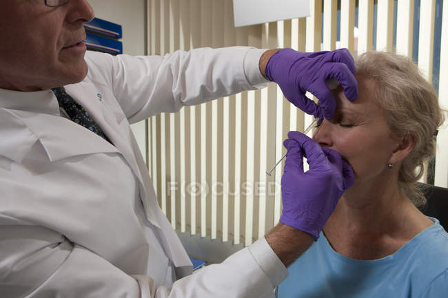 Oftalmólogo que administra una inyección de Botox en la región glabellar de la frente de un paciente - foto de stock