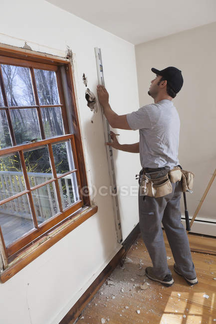 Hispanic carpenter using level to mark cut for new deck doorway in house — Stock Photo