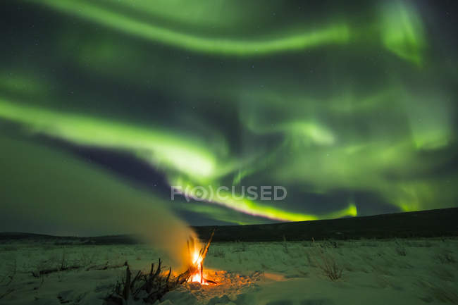 Aurora boreal llena el cielo sobre un fuego de madera a la deriva en el río Delta; Alaska, Estados Unidos de América - foto de stock