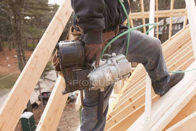 Charpentier avec un pistolet à clous sur le toit de la construction de la maison, image recadrée — Photo de stock