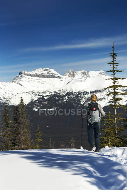 Female hiker on snow-covered pathway with mountains, blue sky and clouds in the background; Lake Louise, Alberta, Canada — Stock Photo