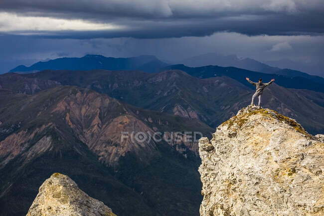 Сонячний промінь, що освітлює мандрівника на вершині гори Сукакпак, як штормові хмари, заварені на відстані над хребтом Брукс; Аляска, Сполучені Штати Америки. — стокове фото