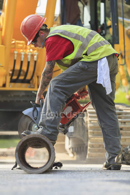 Construction worker cutting water main to length with gas powered saw — Stock Photo